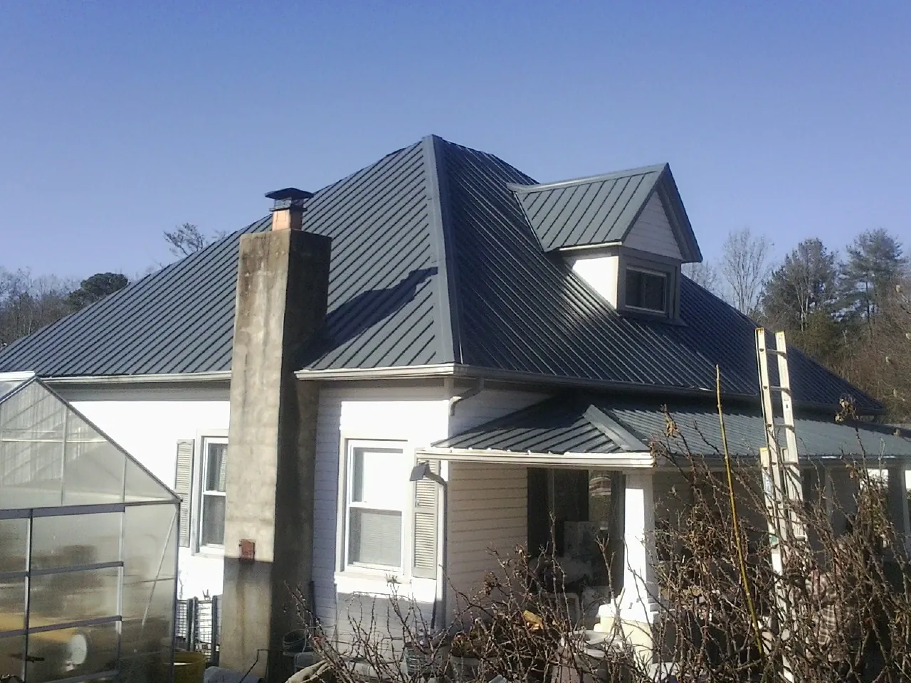 Dark blue standing seam metal roof on a white farmhouse with dormer — Slate & Tile Roof Repair by Roofing Brothers in Hawkeye