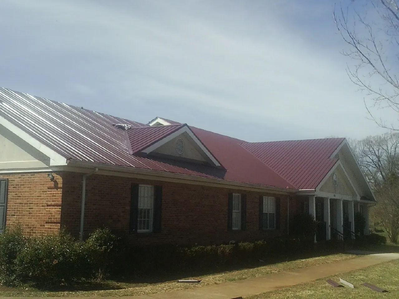 Red metal roof with gabled entries on a long brick building, from a Hail Damage Roof Repair job in Hawkeye