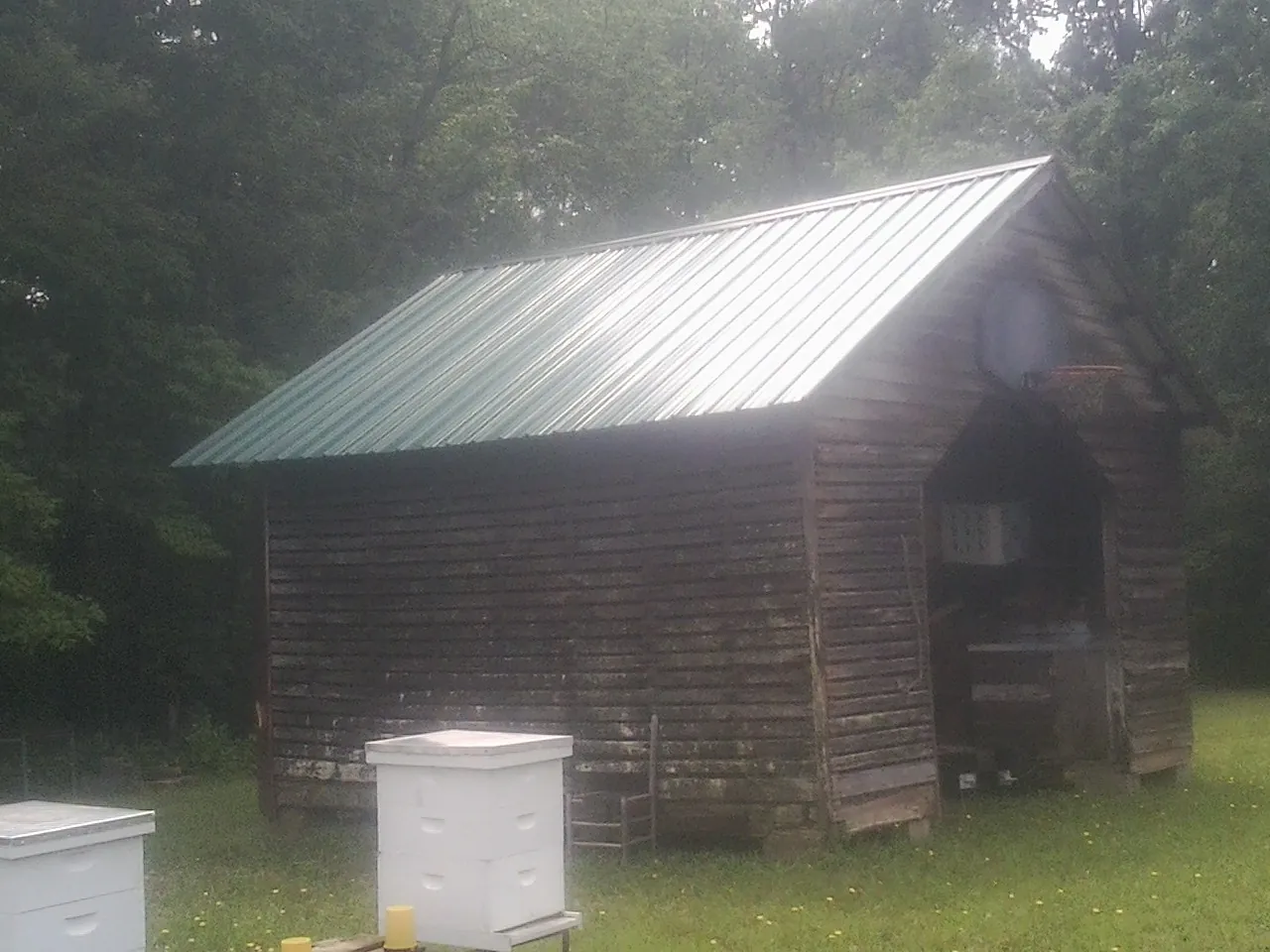 Green metal roof on a weathered barn beside stacked beehives in Hawkeye