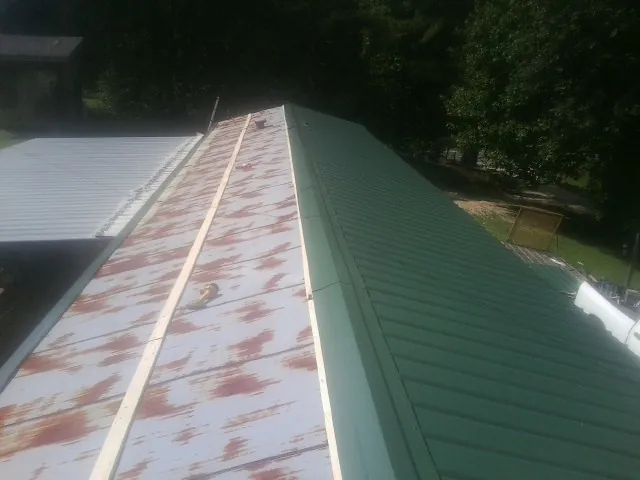 Old rusted panels beside newly installed green metal roofing — Wind Damage Roof Repair by Roofing Brothers in Hawkeye
