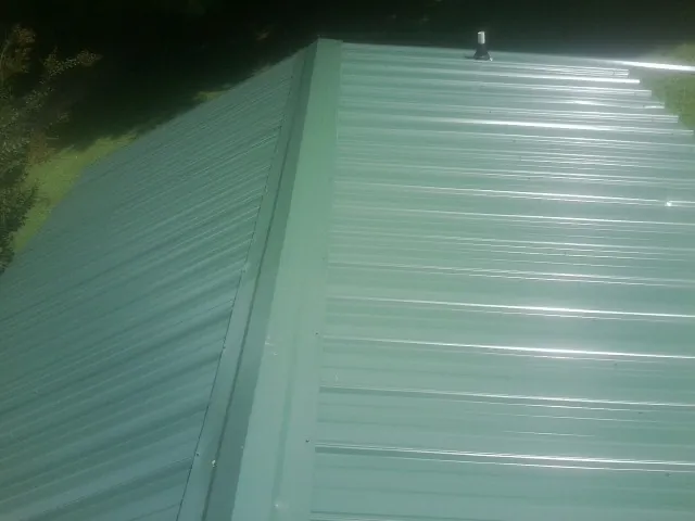 New green metal panels meeting at the ridge of a roof — Flat Roof Repair work by our crew in Hawkeye