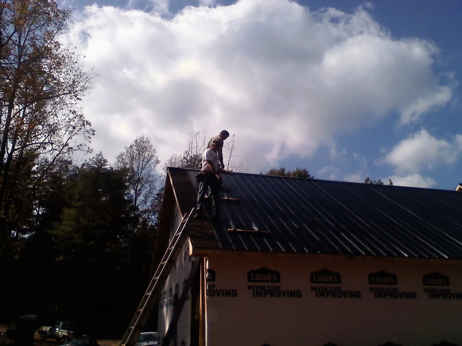 Roofer fastening dark metal panels high against a cloudy sky, from a Roof Inspection job in Hawkeye
