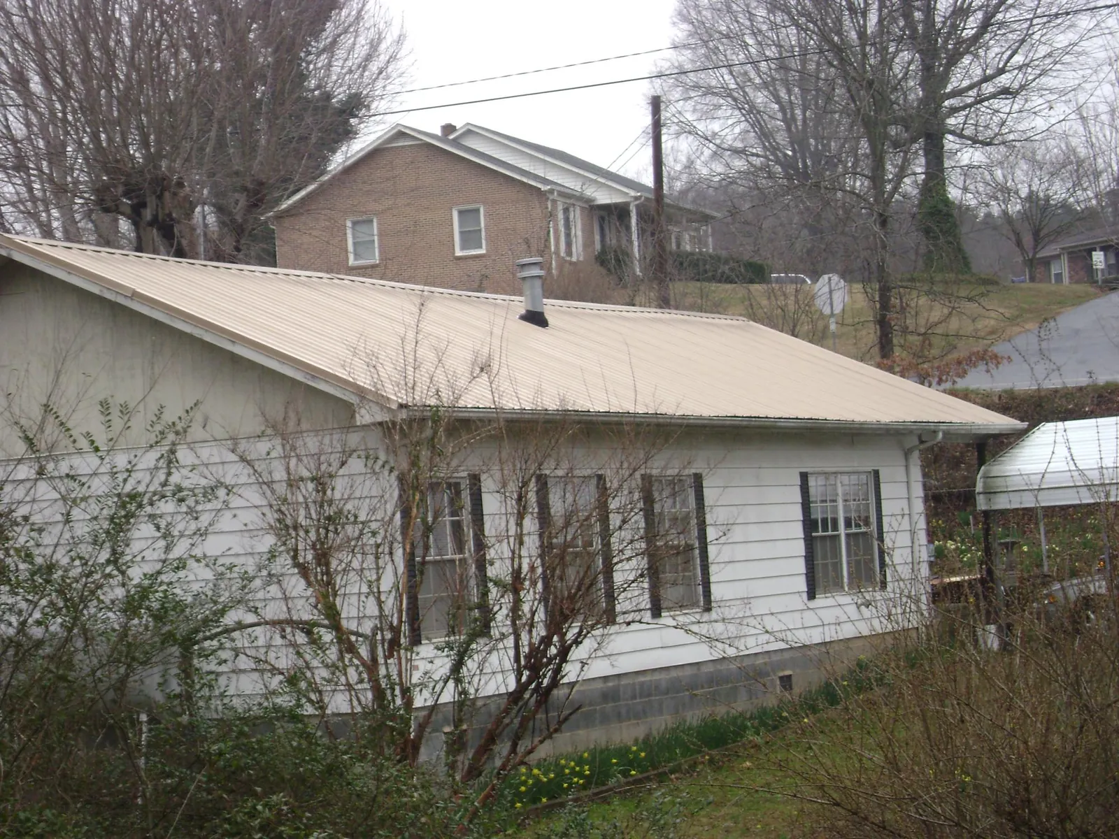 Tan metal roof on a white sided house set into a hillside — Commercial Roofing by Roofing Brothers in Hawkeye