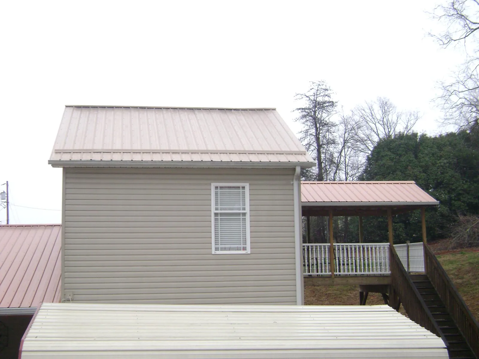 Tan metal roofs on a two story addition and attached porch, from a Roof Replacement job in Hawkeye